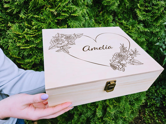 May include: A wooden box with a hinged lid and a brass latch. The lid is decorated with a heart shape and floral designs. The name "Amelia" is engraved inside the heart.